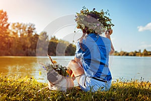 Pug dog and its master chilling by river wearing flower wreaths. Happy puppy and woman enjoying summer nature outdoors