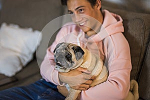 Pug and teenager together hugged on the sofa - pet and domestic dog at home
