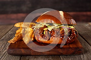 Pulled pork sandwich with potato wedges against wood photo
