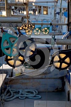Pulleys on a commmercial troller glow in the setting sun, other boats are seen at dock in the background