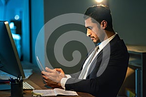 Pulling an all nighter. a young businessman using a digital tablet during a late night at work. photo