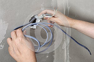 Pulling wires through wall hole, electrician hands close-up.