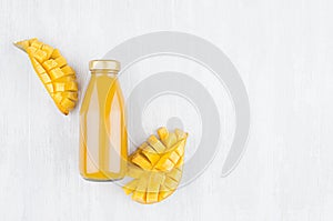 Pulpy fresh mango juice in glass bottle with gold cap, sliced fruit on white wood board, top view, copy space, mock up for design.