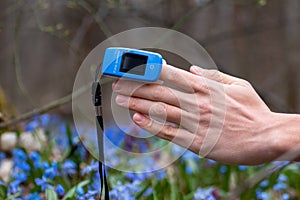 Pulse oximeter on finger close-up in blue flowers