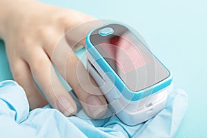 The pulse oximeter shows saturation on a finger on a blue background in the hands of a doctor