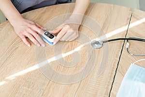 Pulse Oxymeter on a woman finger hand on a wooden table. Top view.