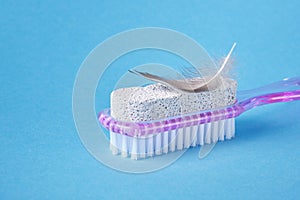 Pumice stone with pink plastic handle and pedicure brush and bird feather on blue background, smooth skin of the foot
