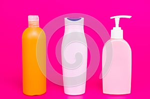 Pump and flip cap plastic containers for liquid cosmetic products in row pink background copy space, bottles