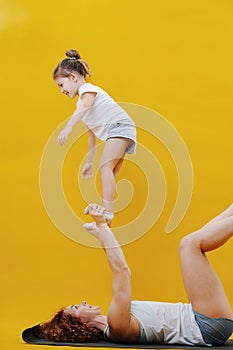 Pumped mom and little daughter doing gymnastics together, standing on feet.