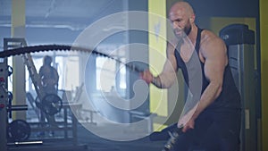 A pumped-up athlete works out in a gym with battle ropes.