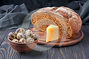 Pumpernickel - bread made with a combination of rye flour and whole rye grains. Quail eggs in a clay bowl, cheese. Fresh healthy