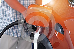 Pumping gasoline fuel in orange car at a gas station. To fill car with fuel in petrol station. Petrol station pump. Sunny