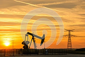 Pumpjack and transmission towers at sunset symbolizing energy transition