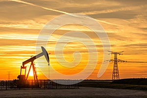 Pumpjack and transmission towers at sunset symbolizing energy transition