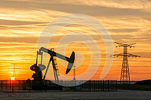 Pumpjack and transmission towers at sunset symbolizing energy transition