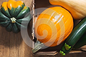Pumpkin, acorn squash, butternut squash, and zucchini close up, wooden background, top view.