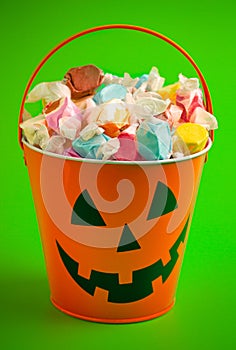 A Pumpkin Bucket Filled with Wrapped Saltwater Taffy on a Bright Green Background