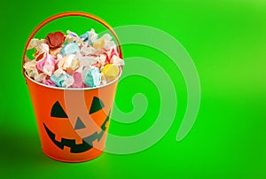 A Pumpkin Bucket Filled with Wrapped Saltwater Taffy on a Bright Green Background