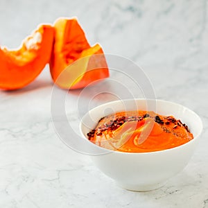 Pumpkin and carrot soup with chili flakes pepper on a white marble background. Copy space. Autumn comfort food concept