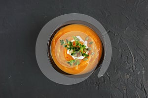 Pumpkin and carrot soup with cream and herbs on dark background.