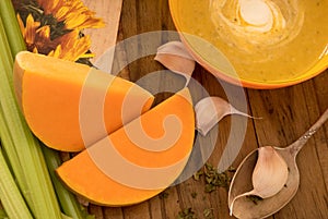 Pumpkin and carrot soup with cream and parsley on dark wooden table with selery, garlick and pieces of pumpkin