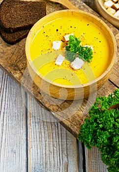 Pumpkin and carrot soup, tadka with cream and parsley on dark wooden background. Top view