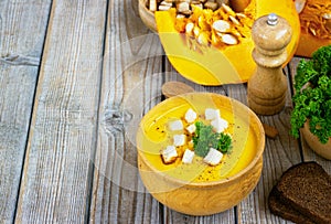 Pumpkin and carrot soup, tadka with cream and parsley on dark wooden background. Top view