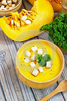 Pumpkin and carrot soup, tadka with cream and parsley on dark wooden background. Top view