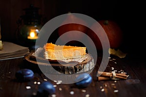 Pumpkin cheesecake, cooked at home, plums, pumpkin, table lamp, vanilla ,notepad, foliage on a wooden dark table. Autumn