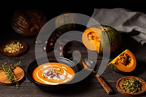 Pumpkin and chestnut soup with cream, pork belly and thyme aside an open pumpkin, chestnuts and bread on dark wood