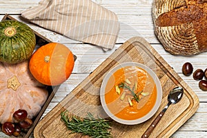 Pumpkin and chestnut soup with rosemary twig aside large bread loaf, cream, entire pumpkins and chestnuts in a crate on wood