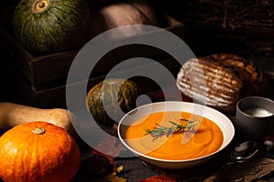 Pumpkin and chestnut soup with rosemary twig aside pumpkins, cream, bread and chestnuts on a vintage dark wood background