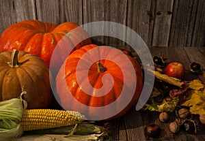 Pumpkin, corn cob, apples, autumn leaves, walnuts and chestnuts on a wooden background.