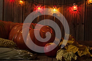 Pumpkin, corn cobs, apple, autumn leaves, colorful lanterns on a wooden background.