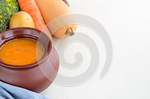 Pumpkin cream soup in a ceramic bowl on a white table. Copy space