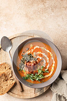 Pumpkin cream soup decorated with cream, pumpkin seeds, bacon, microgreens and olive oil on brown textured background