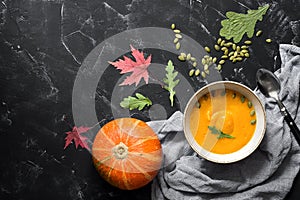 Pumpkin cream soup with seeds on a black stone background decorated with autumn leaves. Diet healthy food. Top view, flat lay,