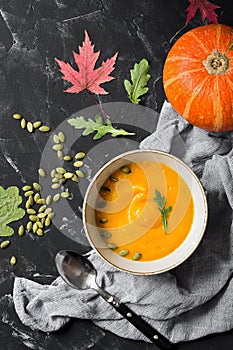 Pumpkin cream soup with seeds on a black stone background decorated with autumn leaves. Vegan and vegetarian lunch and dinner. Top
