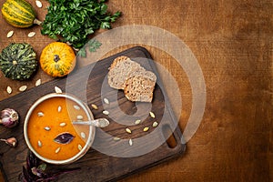 Pumpkin cream soup, served with seed and bread, parsley, basil, on a cutter board. Wooden background.