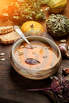 Pumpkin cream soup, served with seed and bread, parsley, basil, on a cutter board. Wooden background.