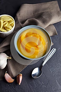 Pumpkin creamy soup with croutons and fresh garlic in ceramic plate with spoon on black background with linen napkin