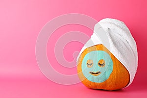 Pumpkin with facial mask and towel on pink background