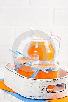 Pumpkin fresh juice in beautiful glasses and jug with pieces of ripe vegetable on white wooden background. Sweet orange juice. Hea