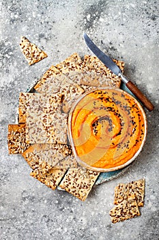 Pumpkin hummus seasoned with olive oil and black sesame seeds with whole grain crackers. Healthy vegetarian appetizer or snack.