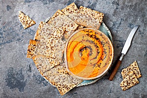 Pumpkin hummus seasoned with olive oil and black sesame seeds with whole grain crackers. Healthy vegetarian appetizer or snack.