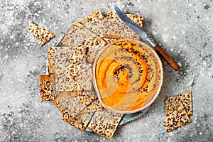 Pumpkin hummus seasoned with olive oil and black sesame seeds with whole grain crackers. Healthy vegetarian appetizer or snack.