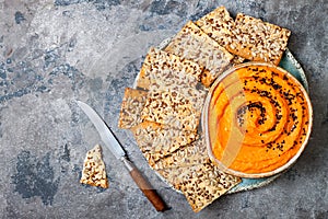 Pumpkin hummus seasoned with olive oil and black sesame seeds with whole grain crackers. Healthy vegetarian appetizer or snack.