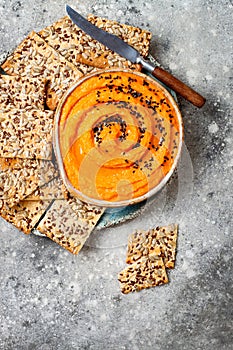 Pumpkin hummus seasoned with olive oil and black sesame seeds with whole grain crackers. Healthy vegetarian appetizer or snack.