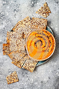 Pumpkin hummus seasoned with olive oil and black sesame seeds with whole grain crackers. Healthy vegetarian appetizer or snack.