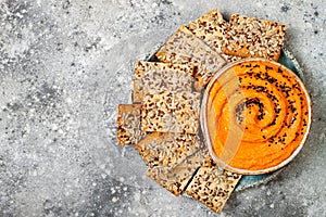 Pumpkin hummus seasoned with olive oil and black sesame seeds with whole grain crackers. Healthy vegetarian appetizer or snack.